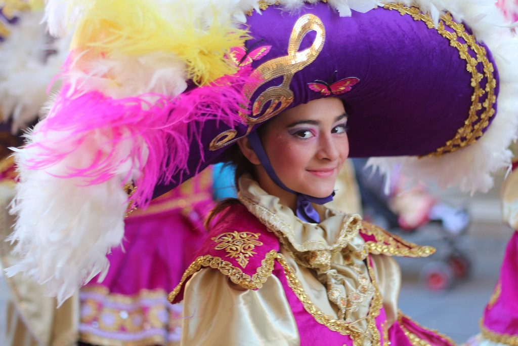 A smiling carnival dancer in a feathered purple hat in Valletta