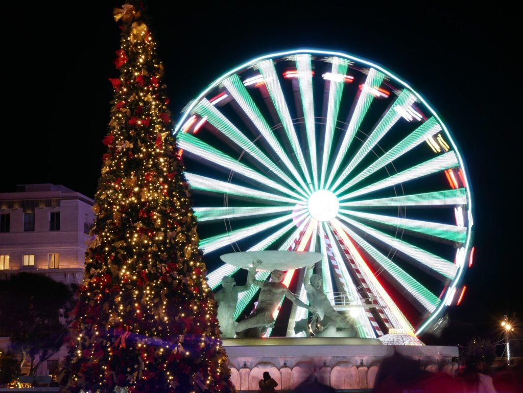 A lit Christmas tree beside a Ferris wheel in Malta at night